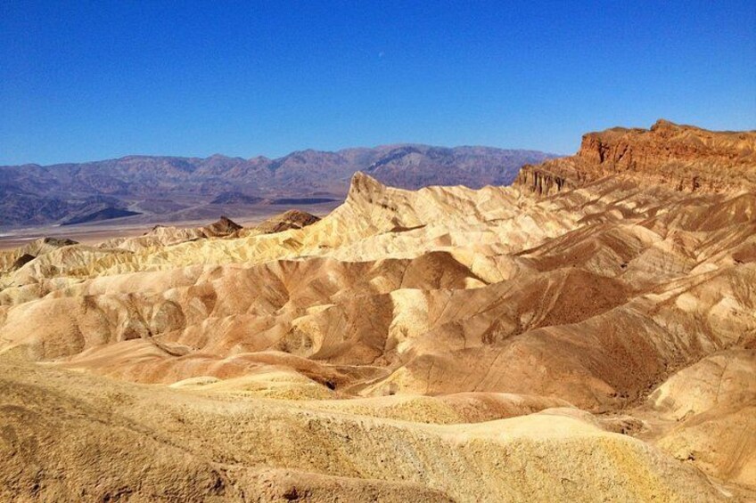 A desert landscape with eroded hills and mountains in the background. 4
