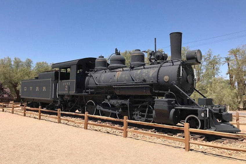 A vintage steam locomotive with the number 2, labeled 'DVRR,' parked on a track with a wooden fence in the foreground. 5