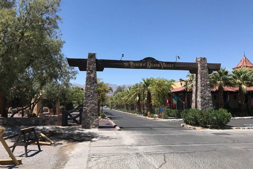 A sign for The Ranch at Death Valley, a paved road, and palm trees. 2