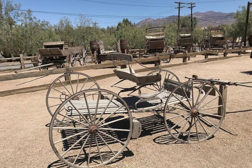 Old wooden wagons and large metal wheels in a desert setting. 2