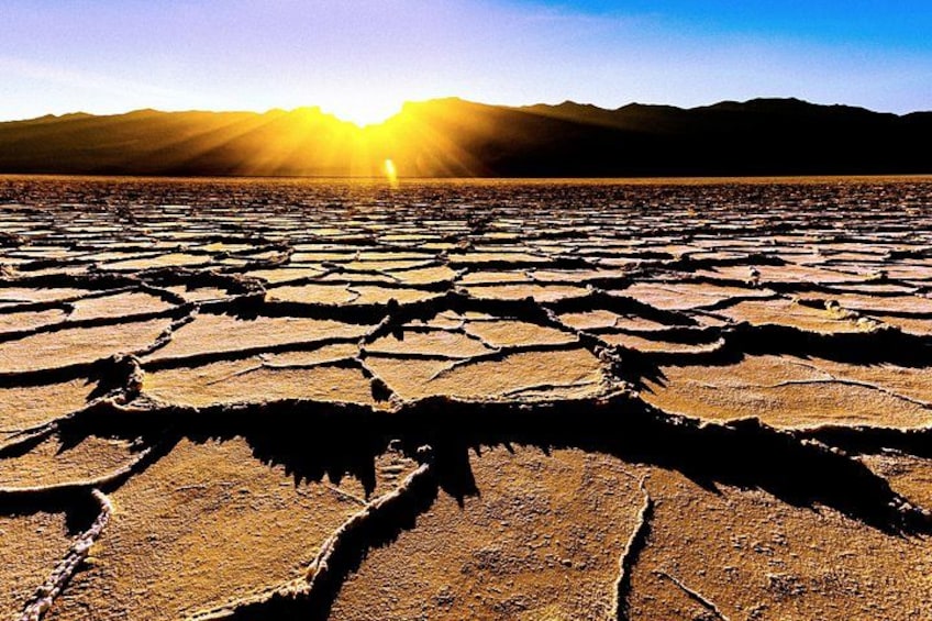 A dry, cracked landscape with a mountain range in the background and the sun setting or rising. 4