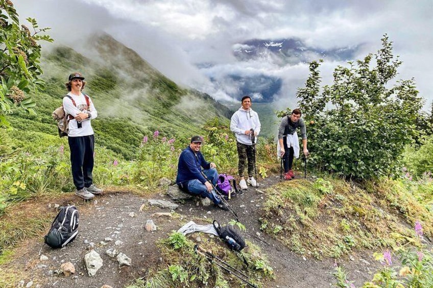 Four people hiking on a mountain trail with backpacks and hiking poles. 2