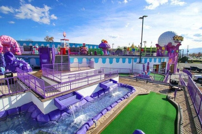 Un parque acuático con estructuras de juego moradas, una zona de césped artificial verde y un edificio esférico grande. 1