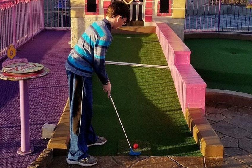 Una persona juega minigolf en un campo de colores brillantes con barreras rosas y amarillas. 3