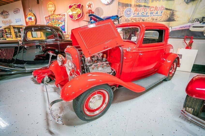 A red vintage car with its hood open, displaying an engine in a museum setting. 5
