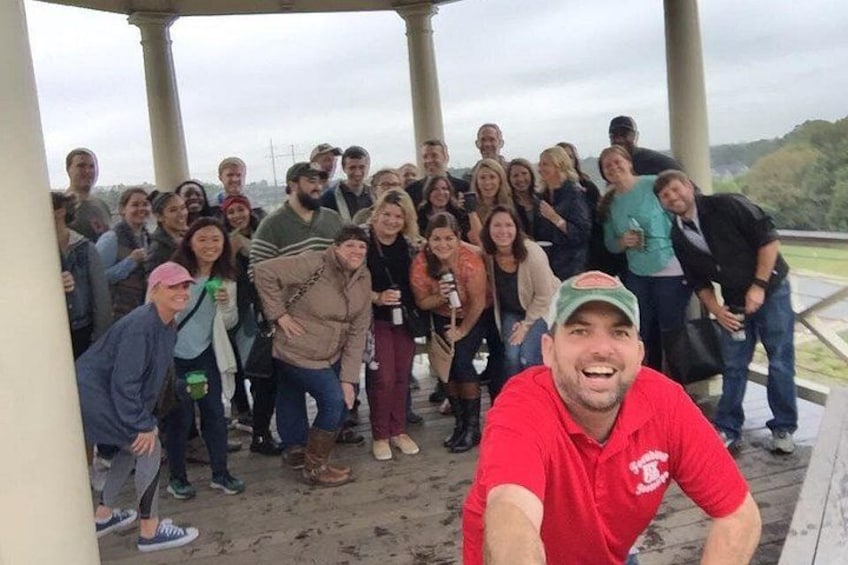 A group of people gathered under a covered area with a view of a hilly landscape. 3