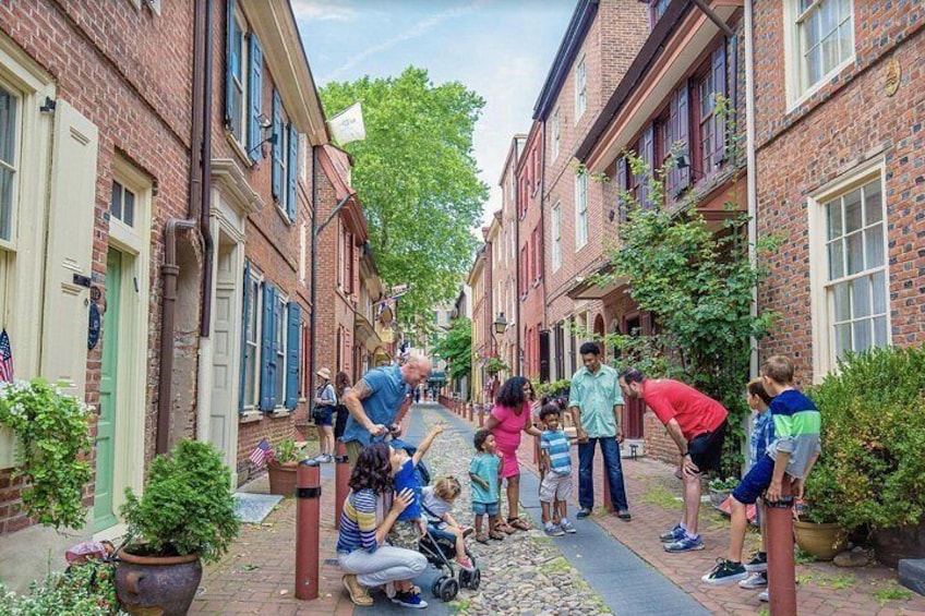 A family interacting with children in a brick-lined street with greenery and a clear sky. 1