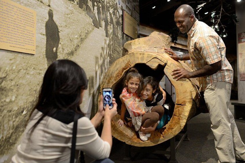 Une grande structure en bois, faite de troncs d’arbres, avec des personnes à l’intérieur, une femme qui prend une photo et un homme qui se tient à côté. 5