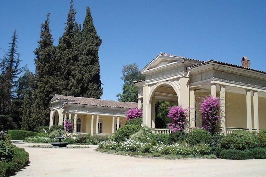 A classical building with columns and a fountain in a landscaped garden. 1