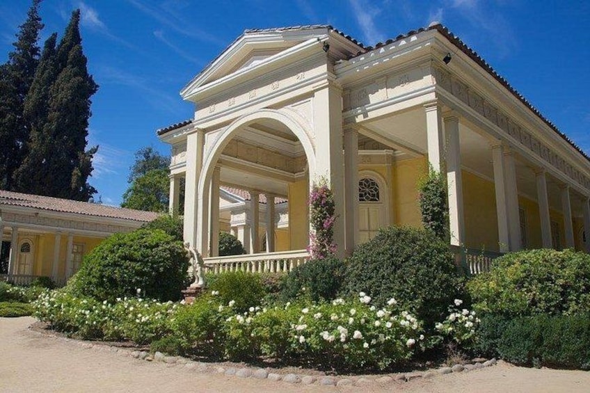 A classical building with columns, a covered porch, and a garden with white flowers. 2