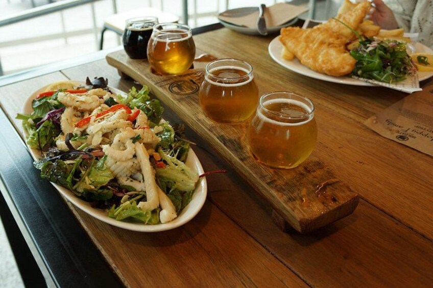 Une table en bois avec une assiette de salade, deux verres de bière et une assiette de poisson-frites. 2