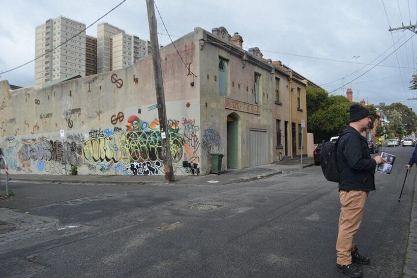 A street with graffiti on a wall, a building with a sign, and a person holding a newspaper. 4