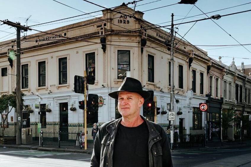A man in a black jacket and hat standing in front of a building with the number 1929. 2