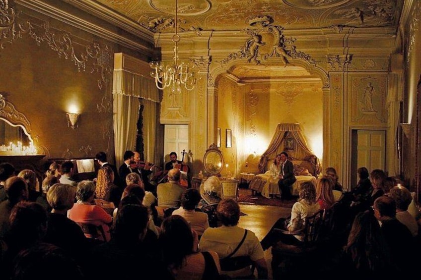 Ein prächtiger Raum mit aufwendiger Dekoration, einer Chandelier und einer Gruppe von Personen, die vor einer Bühne sitzen. 1