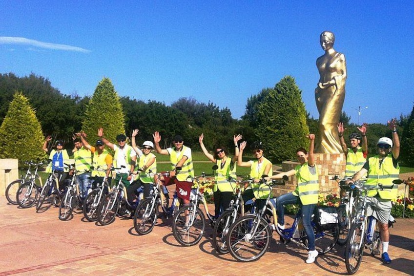 Un gruppo di ciclisti con giubbotti gialli posa accanto a una grande statua dorata in un parco. 1