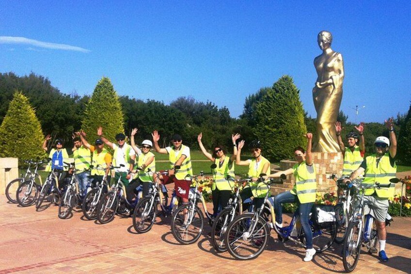 En grupp cyklister i varselvästar poserar tillsammans med en stor gyllene staty i en park. 4