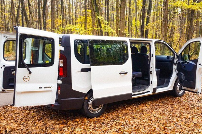 A white van with open doors parked on a leaf-covered ground. 2