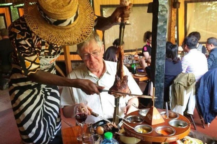 A person serving food to a seated individual at a table with a traditional food serving setup. 4