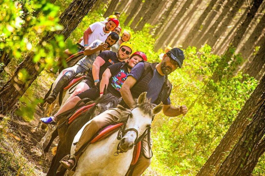 A group of people riding a white horse through a forested area. 1