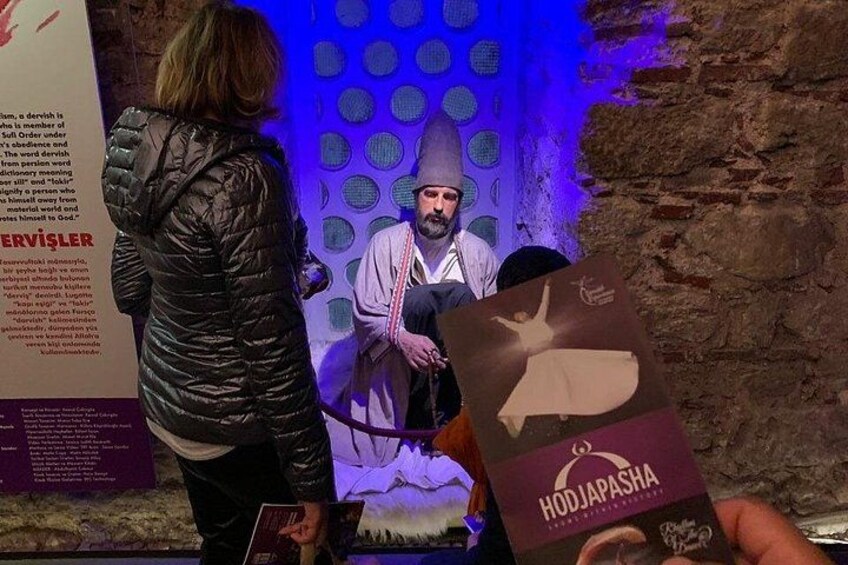 Una persona sostiene un libro titulado 'HODI JAPASHA' frente a un muro de piedra con un fondo iluminado en azul. 1
