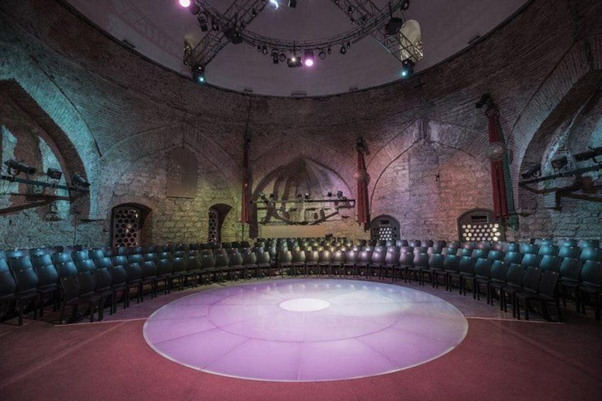 Un auditorio interior con un escenario circular, hileras de sillas y paredes de ladrillo en arco. 5