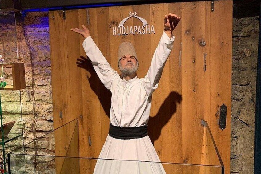 Una persona vestida con traje tradicional frente a un fondo de madera con el texto 'HODJAPASHA' a la vista. 2