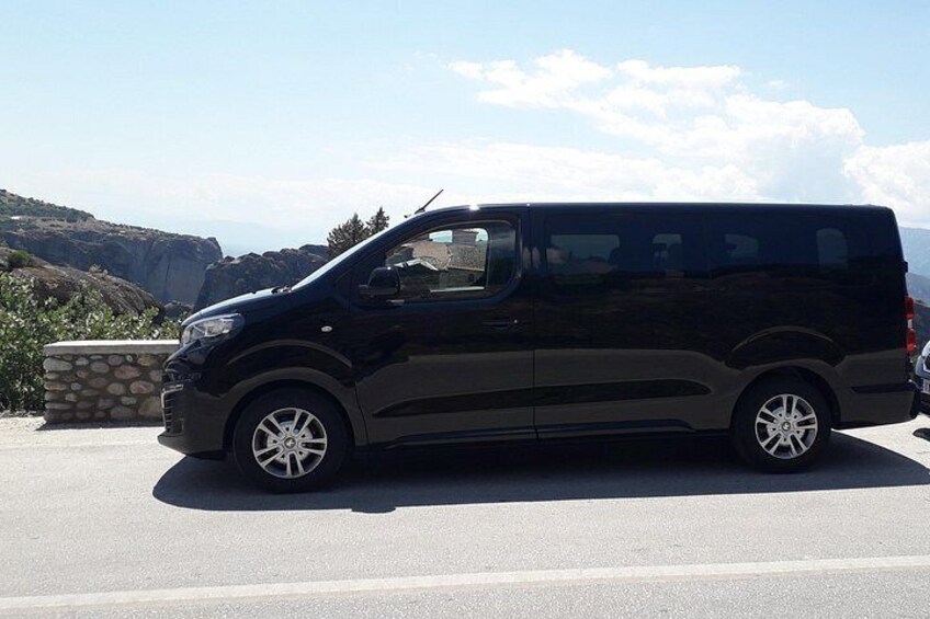 Una camioneta negra estacionada en una carretera, con un muro de piedra y colinas rocosas al fondo. 3