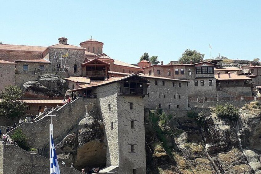 Un edificio de piedra histórico con una torre, rodeado de otras construcciones y terreno rocoso. 2