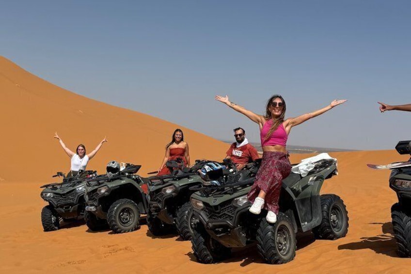 Four people on ATVs in a desert with sand dunes. 1