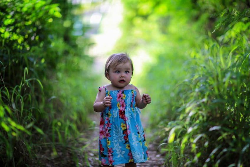 A child in a floral dress walking on a path surrounded by greenery. 3