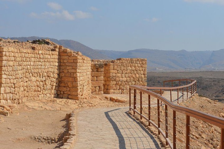 Vestiges d’anciens bâtiments en pierre, avec un chemin pavé et une rambarde en métal. 1