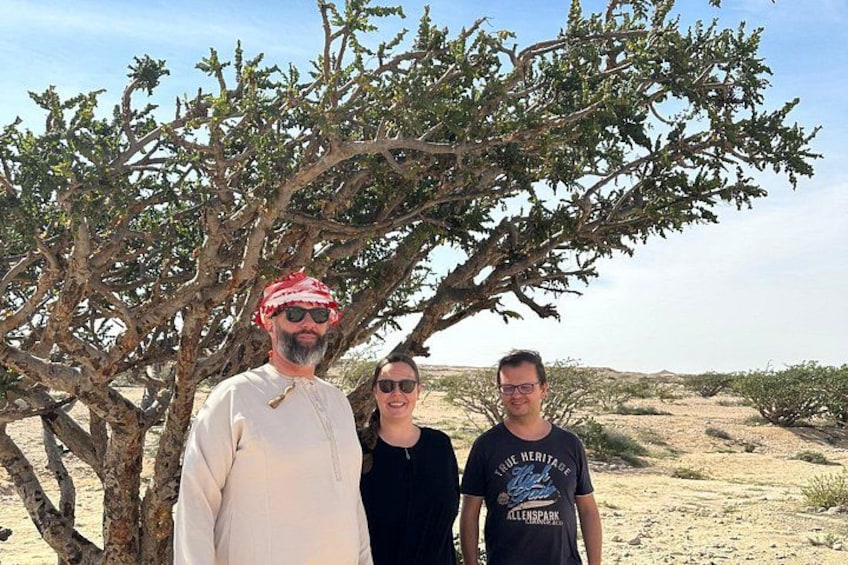 Trois personnes se tiennent debout dans un paysage désertique, avec une végétation clairsemée et un ciel dégagé. 2