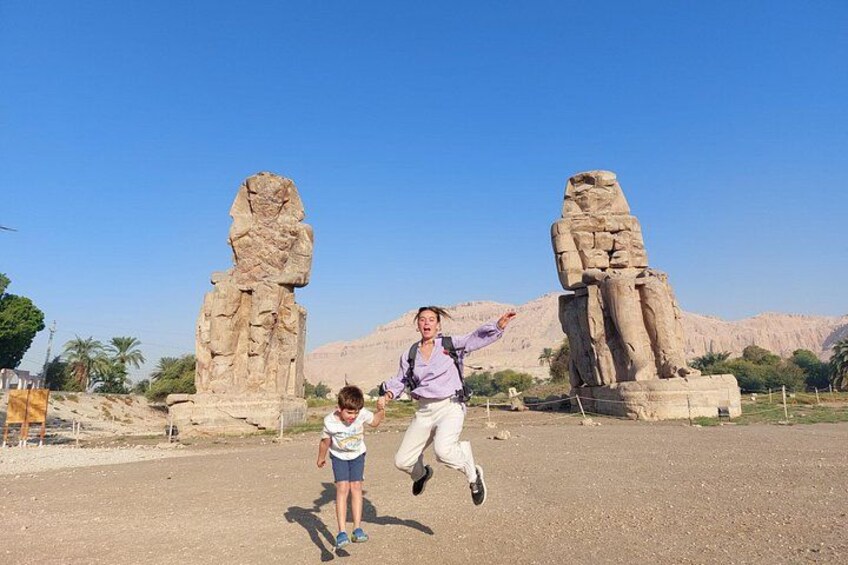 A person jumping in front of two large stone statues. 5