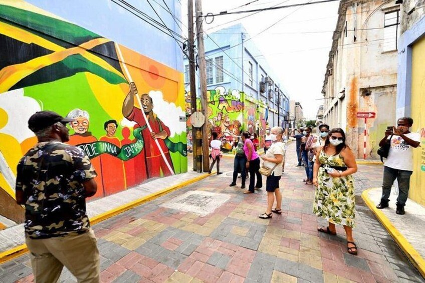 A street with a colorful mural, pedestrians, and a person taking a photo. 1