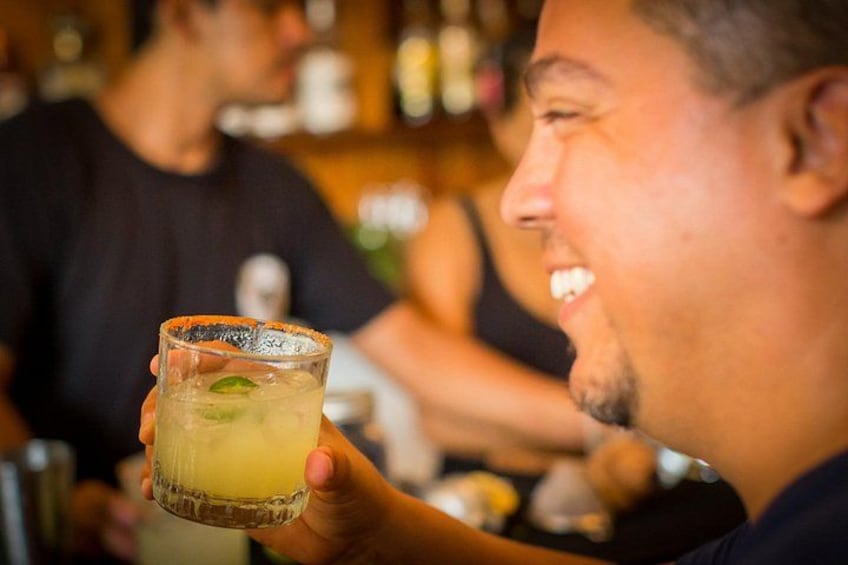 Eine Person hält ein Glas mit einem gelblichen Getränk, vermutlich ein Cocktail, in einer Bar. 3