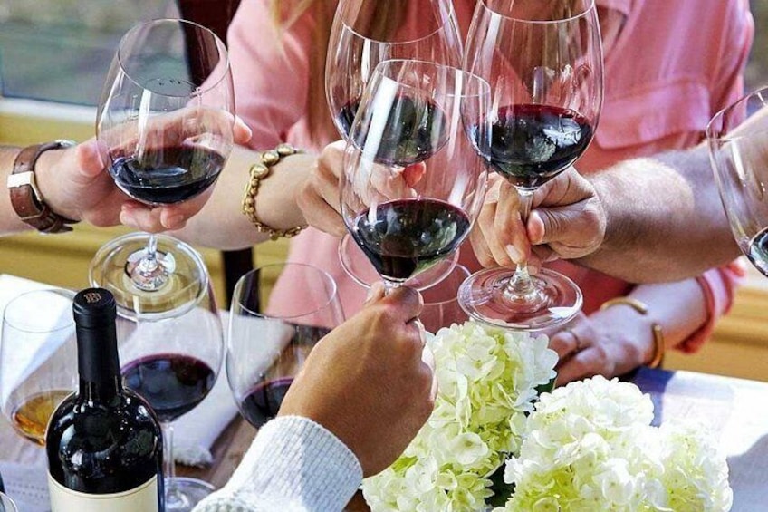 Personas brindando con copas de vino, una botella y un ramo de flores sobre una mesa. 2
