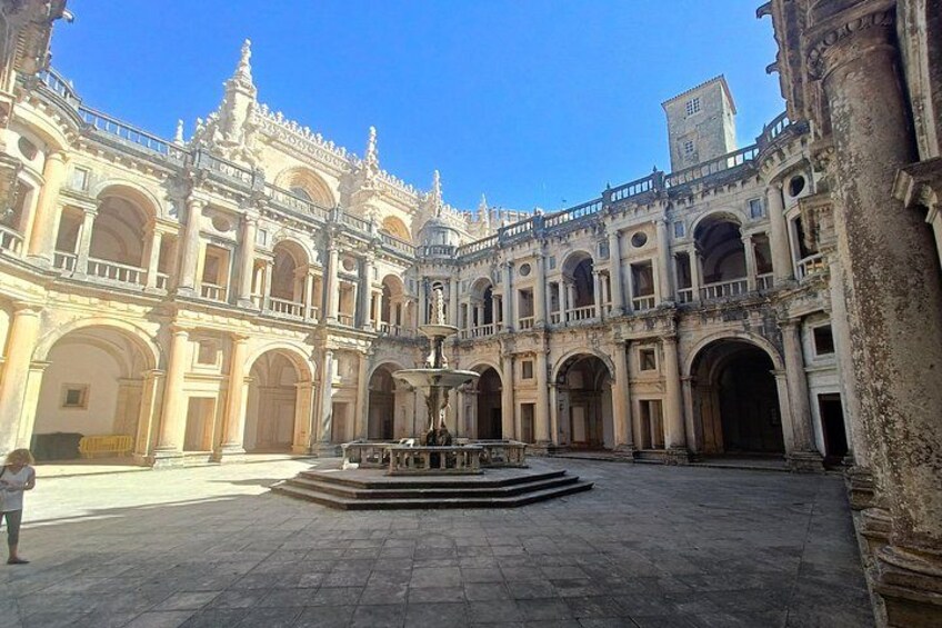 A grand courtyard with ornate architecture, a central fountain, and a clear blue sky. 3