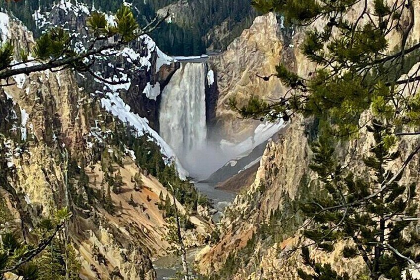 A waterfall in a canyon with snow on the cliffs and trees in the foreground. 4