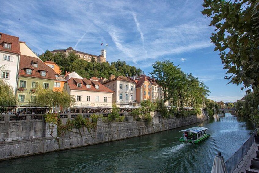 A river with a boat, buildings along the riverbank, and a hill with a tower in the background. 3