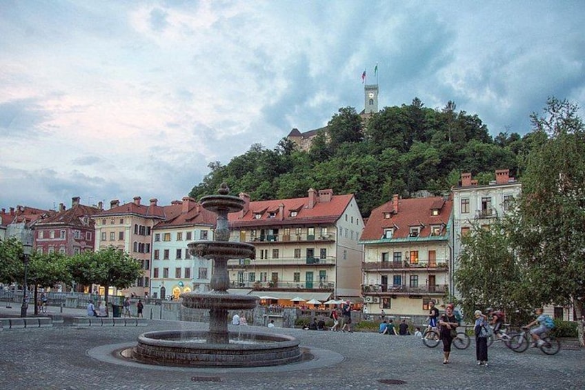 A historic square with a central fountain, surrounded by colorful buildings and a hill with a tower in the background. 5