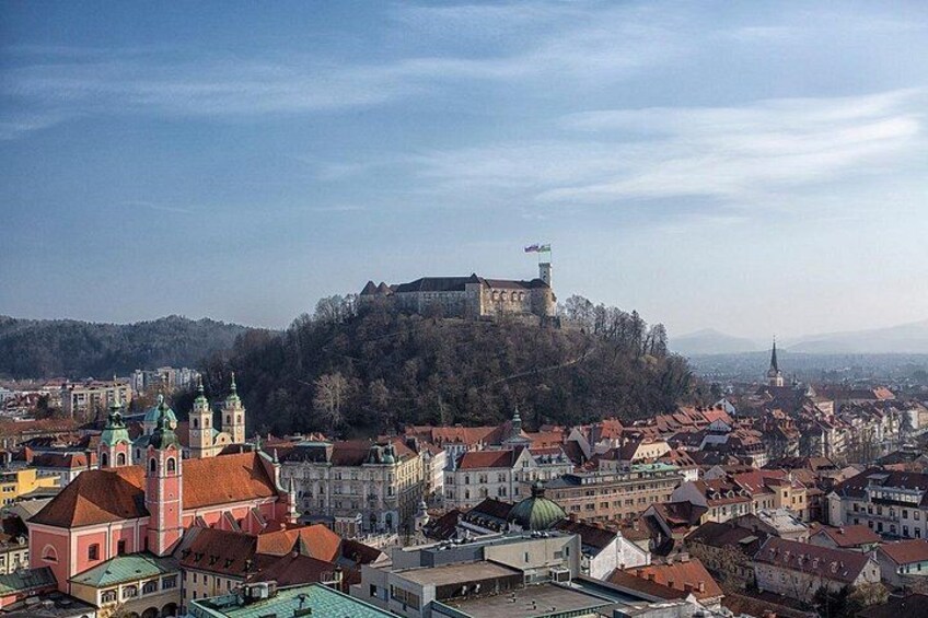 A historic city with a prominent castle on a hill, colorful buildings, and a church with a green dome. 2