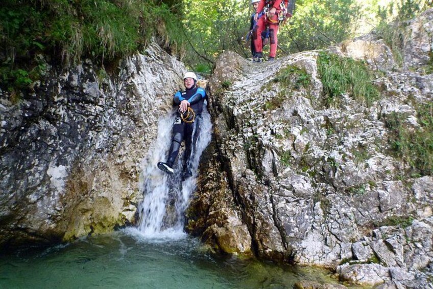 Una persona descendiendo en rápel por un risco hasta una piscina de agua cristalina. 2