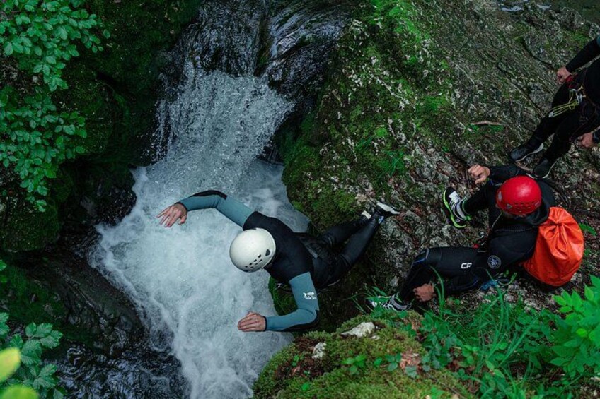 Una persona con traje de neopreno y casco cerca de una cascada en un área boscosa. 3