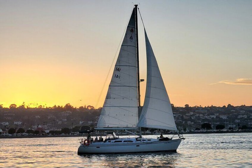 Un voilier avec une grande voile naviguant sur une étendue d’eau au coucher du soleil. 3