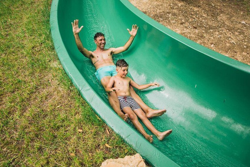 Two people sliding down a green slide in a grassy area. 3