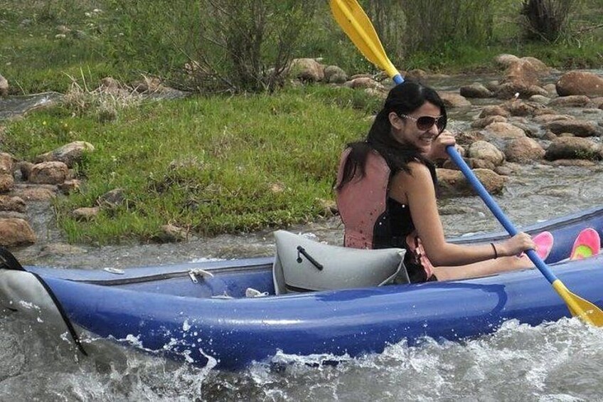 A person in a blue kayak on a river with rocks and greenery in the background. 1