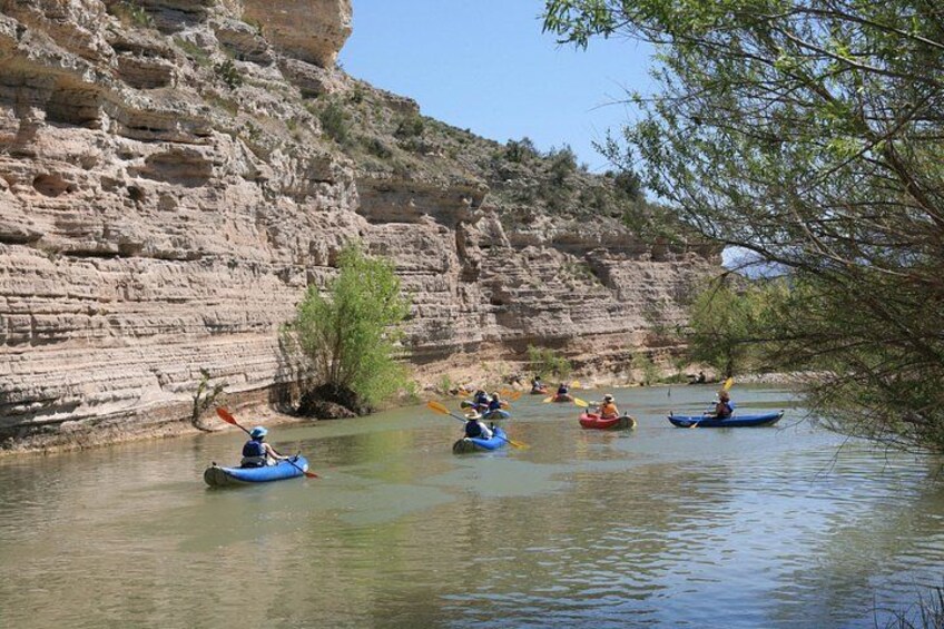 Kayakers on a calm river with rocky cliffs in the background. 3