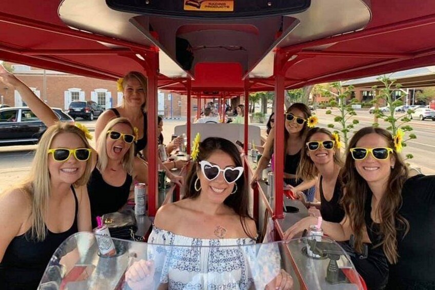 Un groupe de personnes est assis autour d’une table à l’intérieur d’un véhicule rouge, vraisemblablement un autobus ou un tramway, d’où la rue est clairement visible. 1