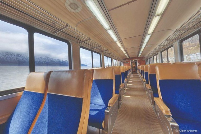 Interior de un tren con asientos azul y marrón, paneles de madera y ventanas amplias. 3
