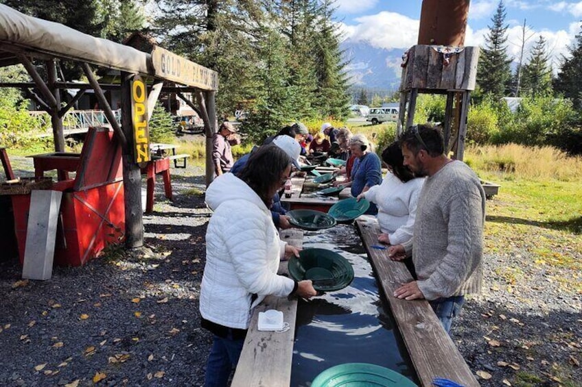 People preparing food outdoors at a picnic area with wooden tables and a red structure labeled "GOLD POND." 1